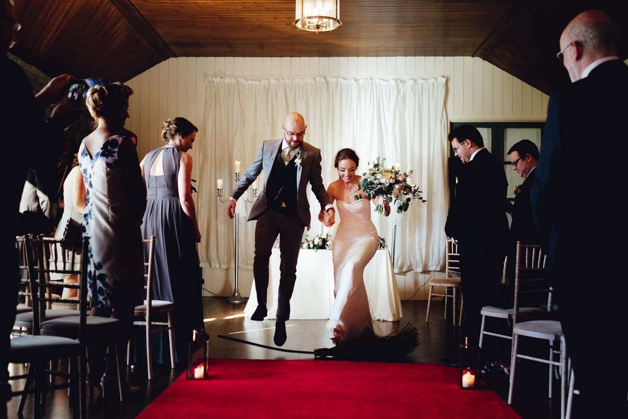 bride and groom jump over a broom and the end of their wedding ceremony