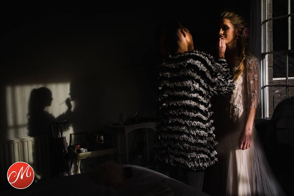 makeup artist applies the finishing touches to the bride
